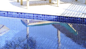 Una piscina con detalles en azulejos azules y sillas de descanso con cojines verdes.