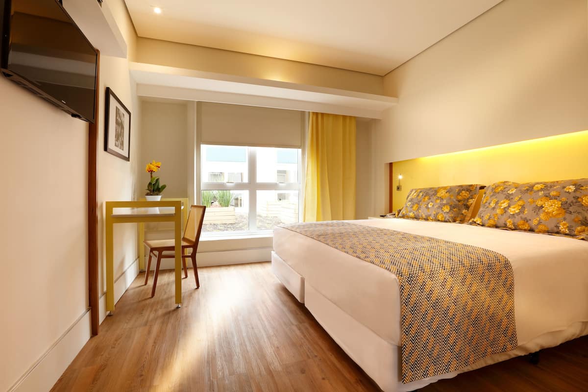 Una habitación de hotel con cama, escritorio y ventana con cortinas.