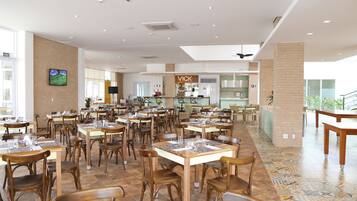 A spacious restaurant with multiple tables and chairs, a visible counter area, and a television screen mounted on the wall.