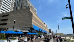 Un muelle con gente caminando, mesas al aire libre y un edificio con una bandera estadounidense.