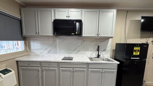 Una cocina con armarios blancos, un microondas negro, un refrigerador negro y un ventanal con vistas.