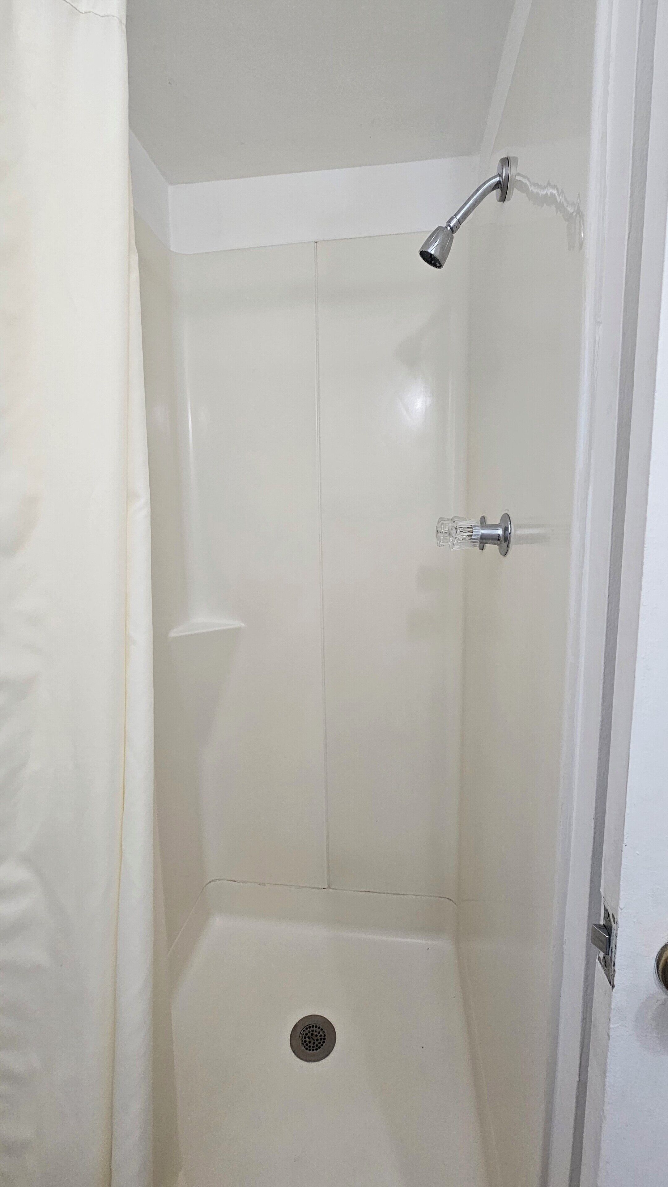 A small, white, tiled shower stall with a showerhead and a drain.