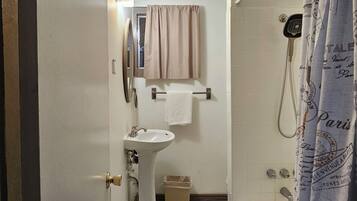 A narrow bathroom with a sink, mirror, and shower.