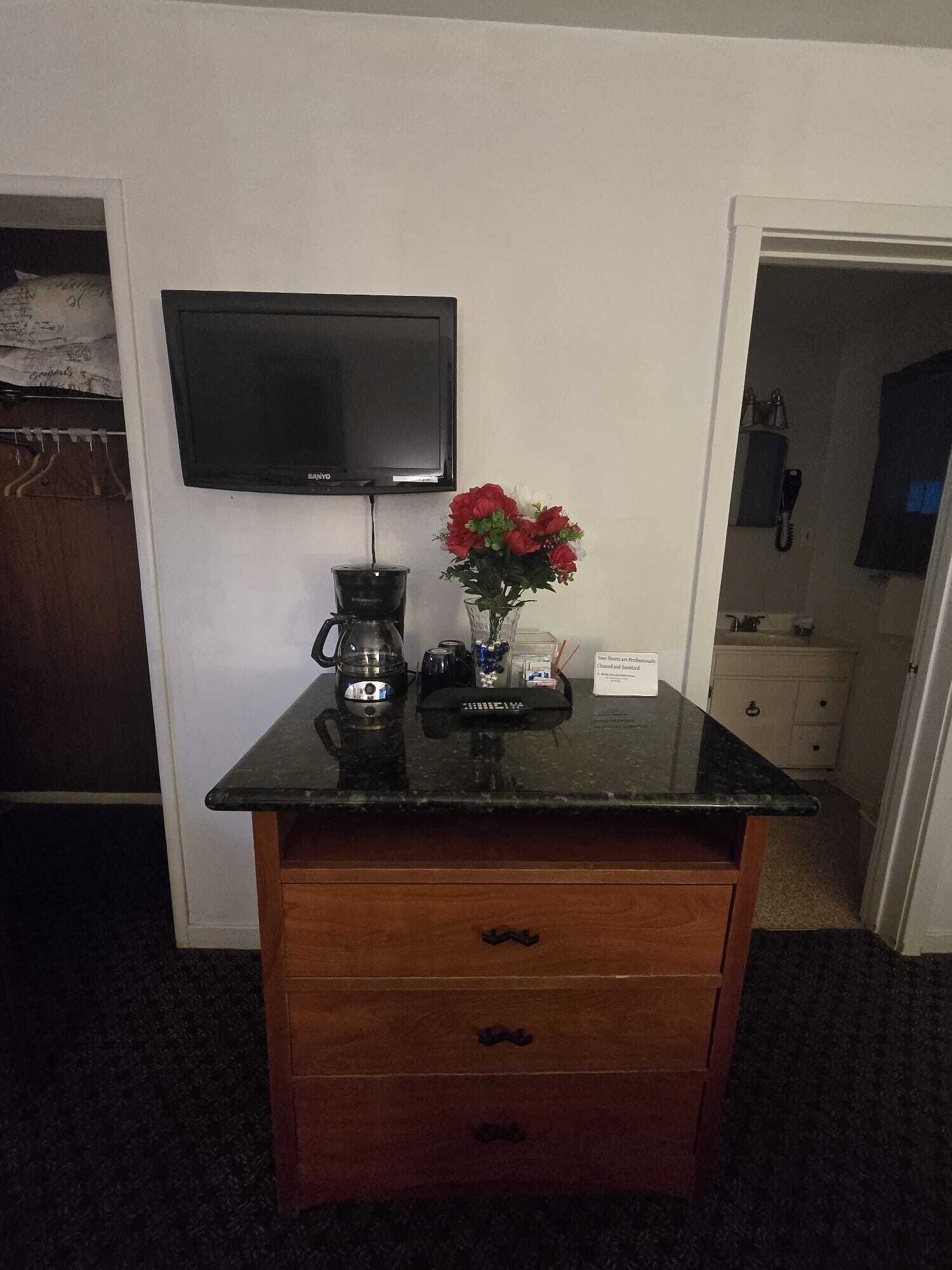 A small kitchenette with a coffee maker, a vase with flowers, and a flat-screen TV mounted on the wall.
