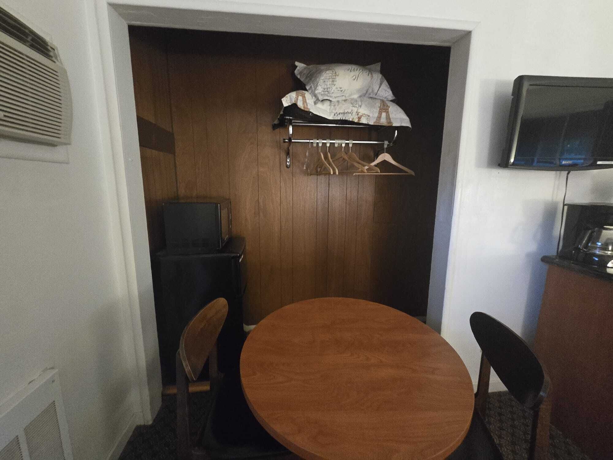 Een kleine kamer met een houten deur, een televisie, een tafel met stoelen en een kapstok met ophangers.