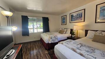 A hotel room with two beds, a TV, a window with curtains, and framed pictures on the wall.