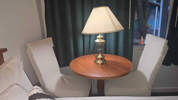 Une chambre d’hôtel comprenant un lit, deux fauteuils rembourrés, une petite table en bois avec une lampe et une fenêtre avec des rideaux.