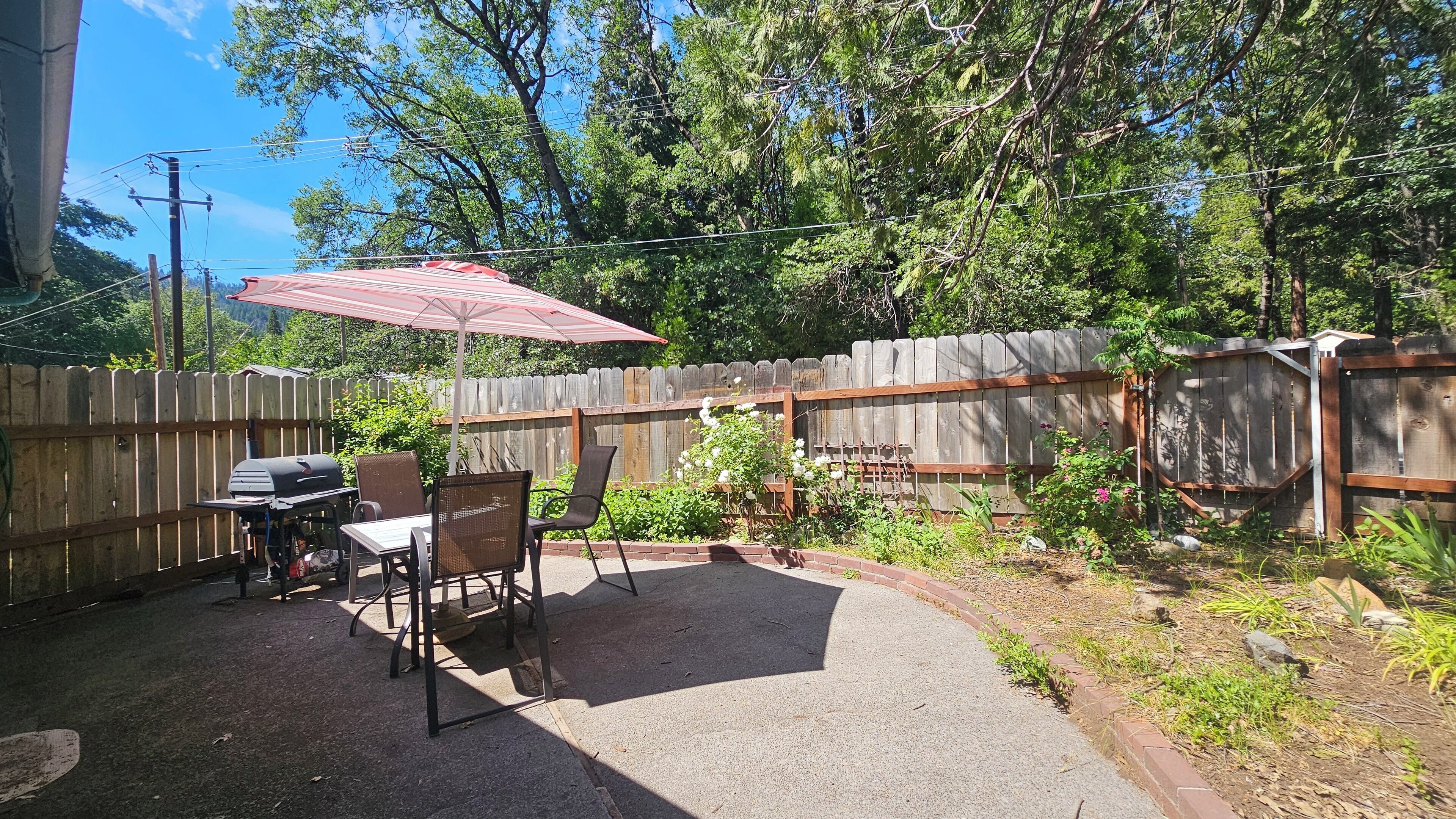 An outdoor patio with a grill, chairs, and a table under a red umbrella.