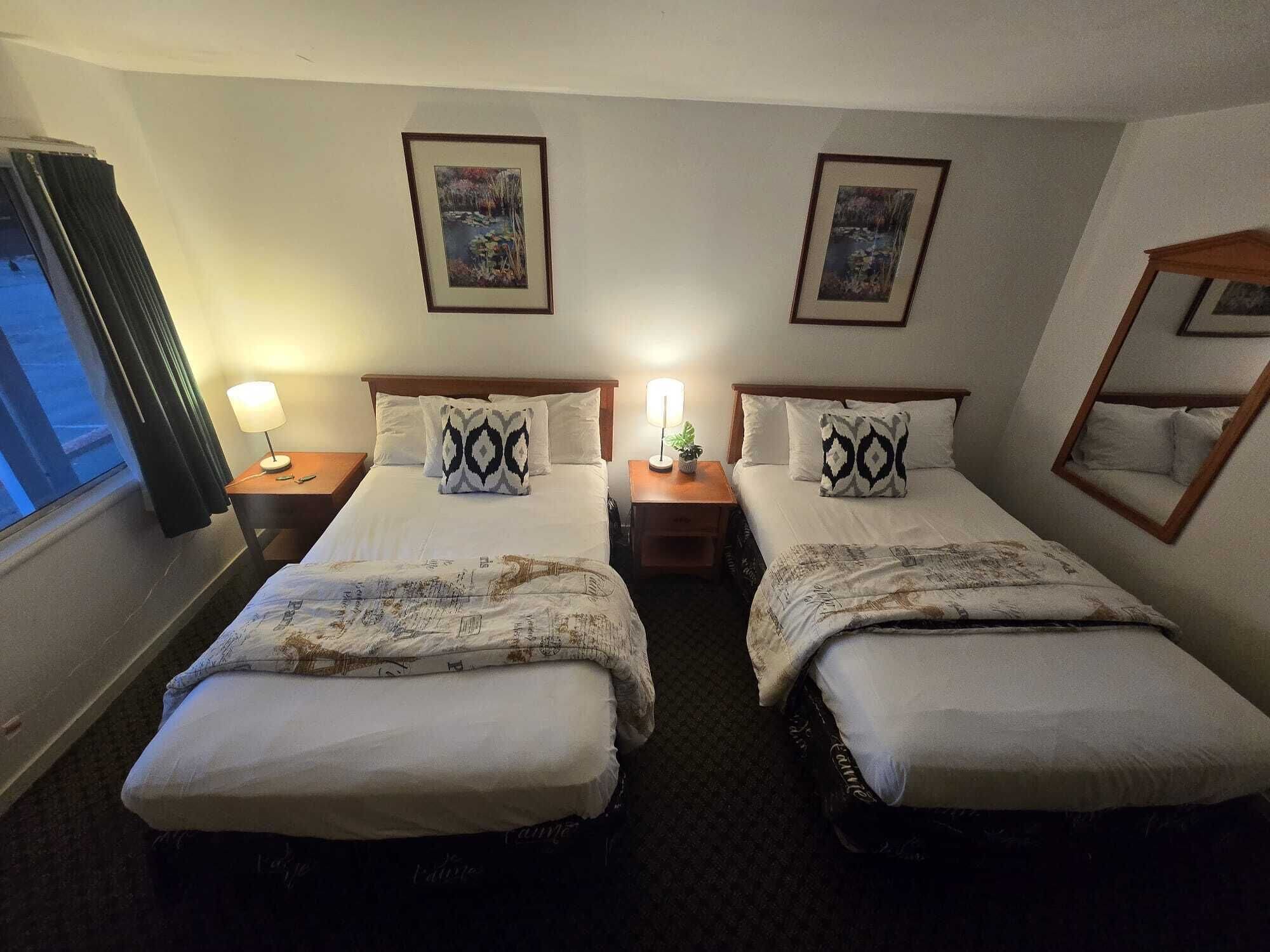 A hotel room with two beds, each with a patterned bedspread, two bedside lamps, and framed pictures on the walls.