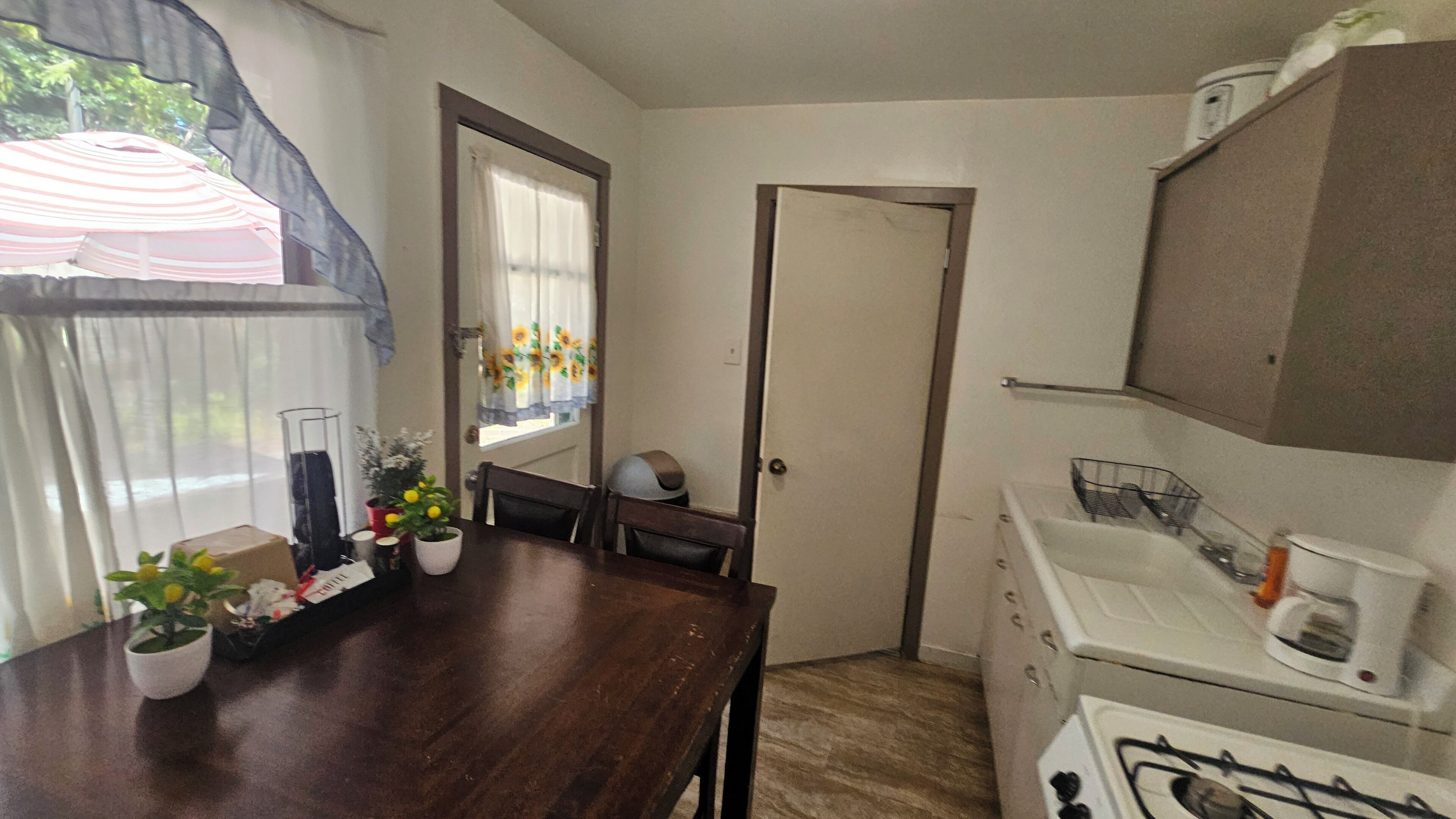 A compact kitchen with a wooden table, a gas stove, and a window with curtains.