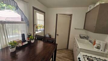 A compact kitchen with a wooden table, a gas stove, and a window with curtains.