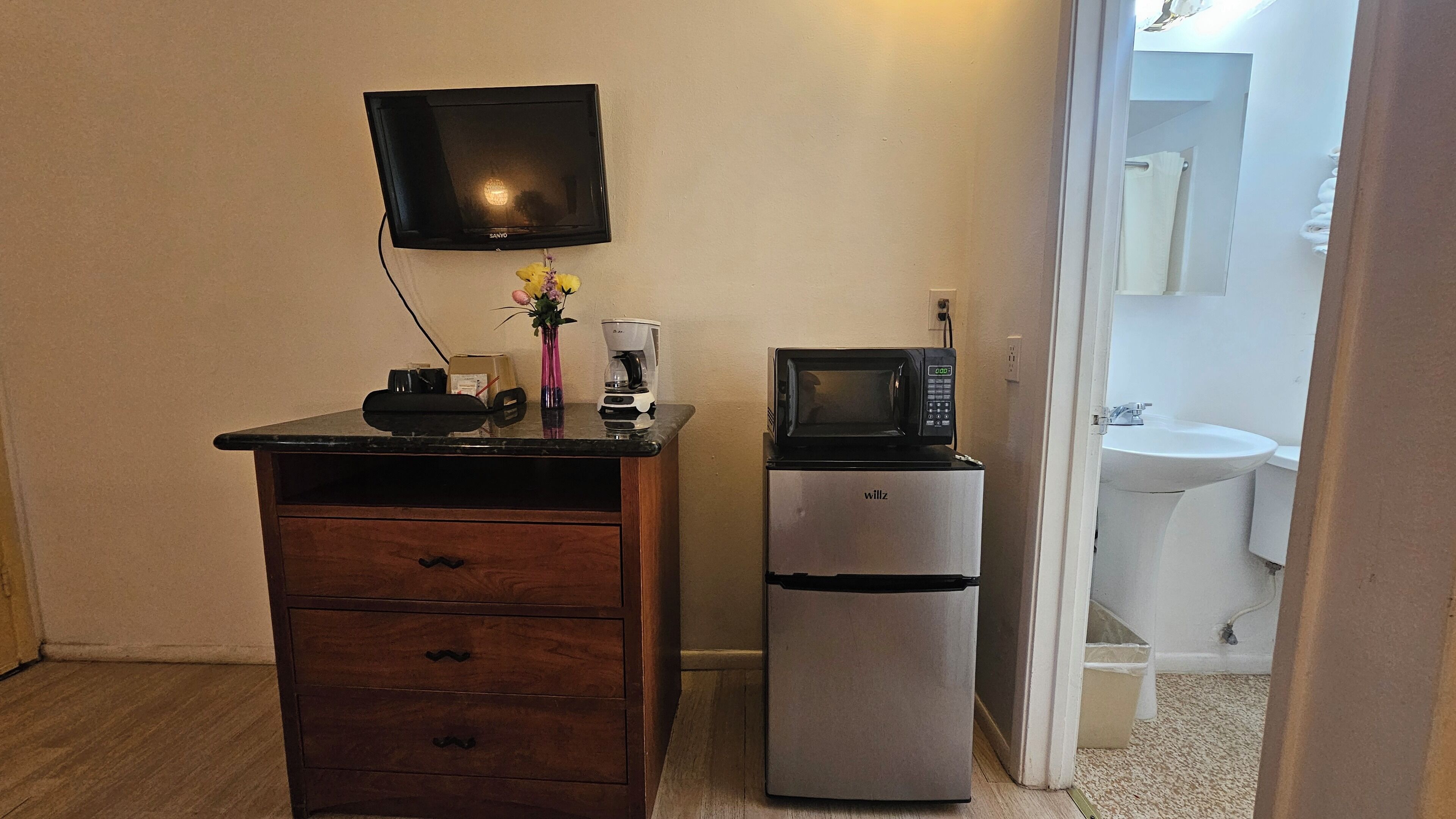 A compact kitchenette with a microwave, a small refrigerator, a coffee maker, and a television on a wooden cabinet.