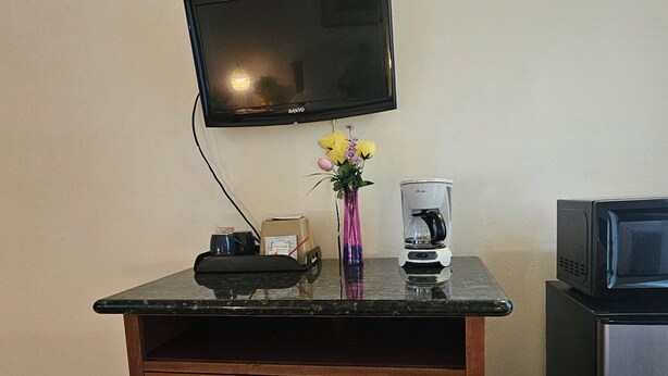 A small kitchenette with a flat-screen TV, a coffee maker, a microwave, and a wooden cabinet with drawers. - Cedar Lodge Motel (Dunsmuir)
