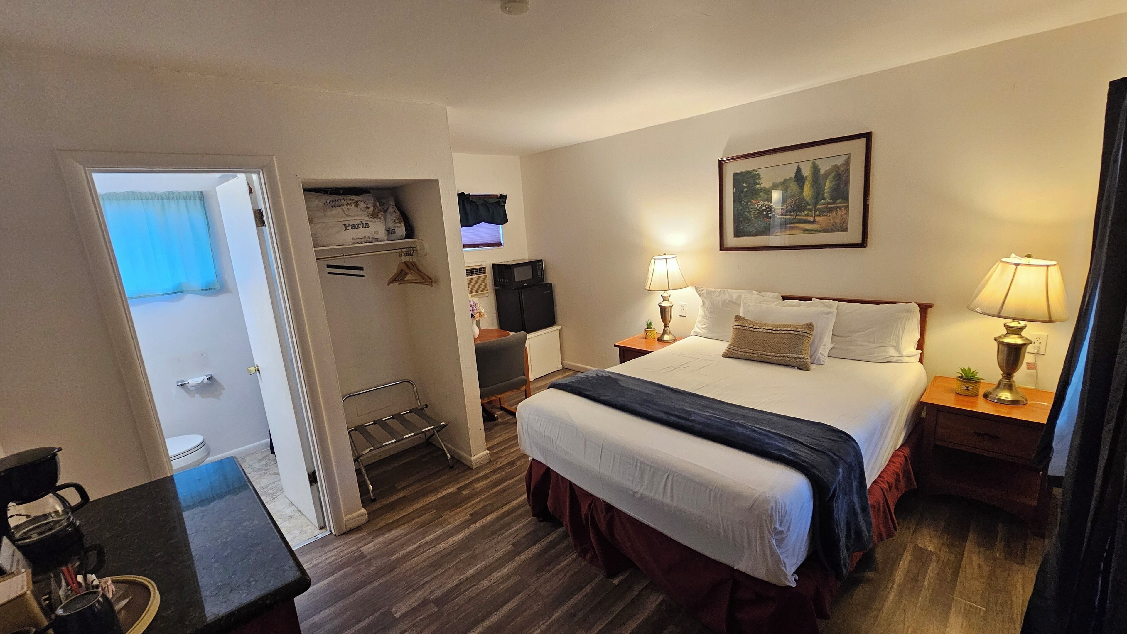 Ein Hotelzimmer mit Bett, Nachttischen, einem Schreibtisch mit Stuhl, einem Kleiderschrank und einem Badezimmer.
