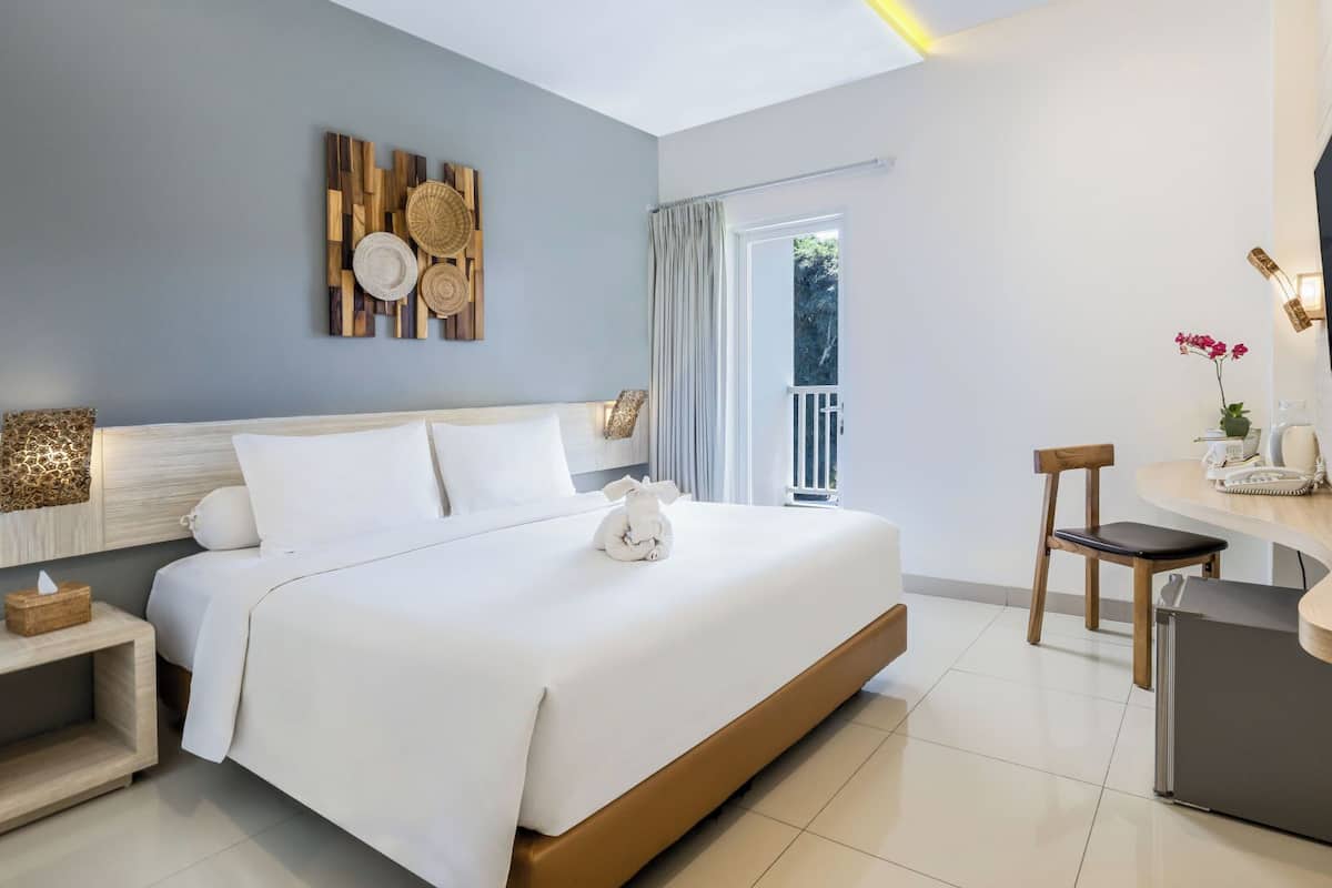 Habitación de hotel moderna con una cama grande, un escritorio, un televisor y un balcón con cortinas.