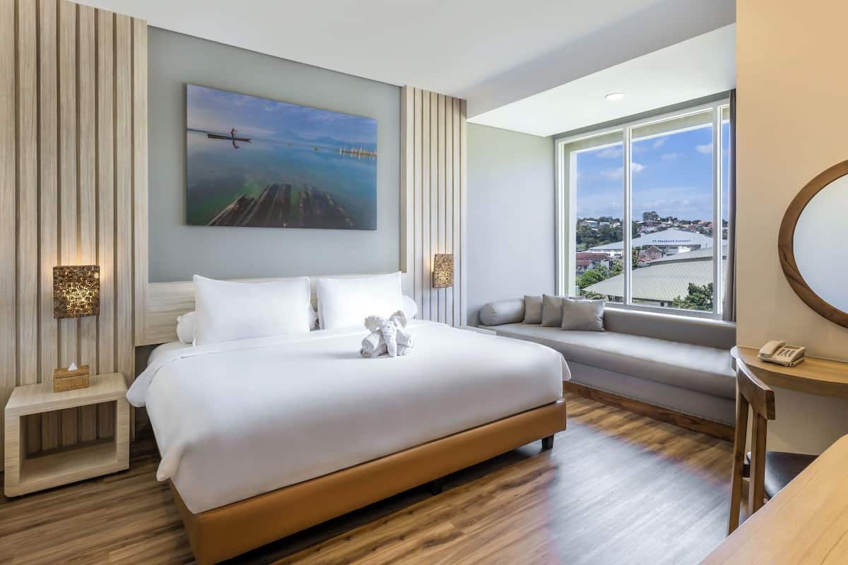 Habitación de hotel moderna con una cama grande, vistas de la ciudad, un espejo redondo y una mesita con un teléfono.