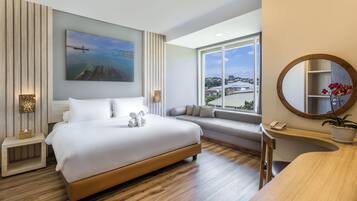 A modern hotel room with a large bed, a view of the city, a round mirror, and a small table with a phone.