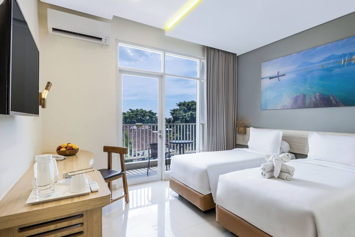 Habitación de hotel con dos camas, un escritorio con silla, un televisor y un ventanal con vistas al exterior.