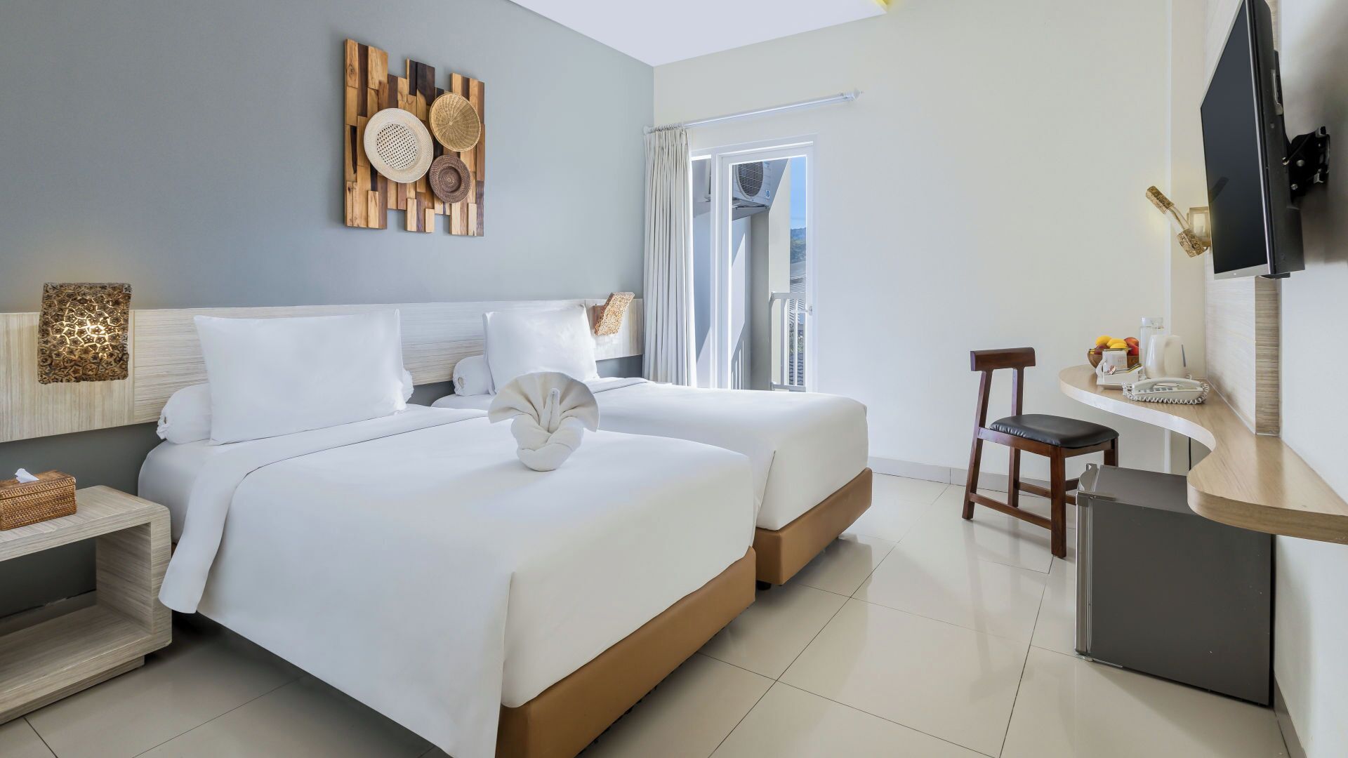 A hotel room with two beds, a desk, a chair, a TV, and a window with curtains.
