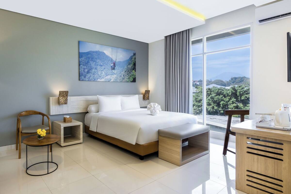 Habitación de hotel moderna con una cama grande, un escritorio, una silla, una mesita de noche y vistas al exterior.