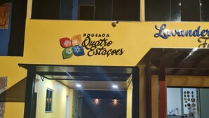 Un bâtiment à la façade jaune, une enseigne indiquant « Pousada Quatro Estações » et un espace d’entrée abrité.