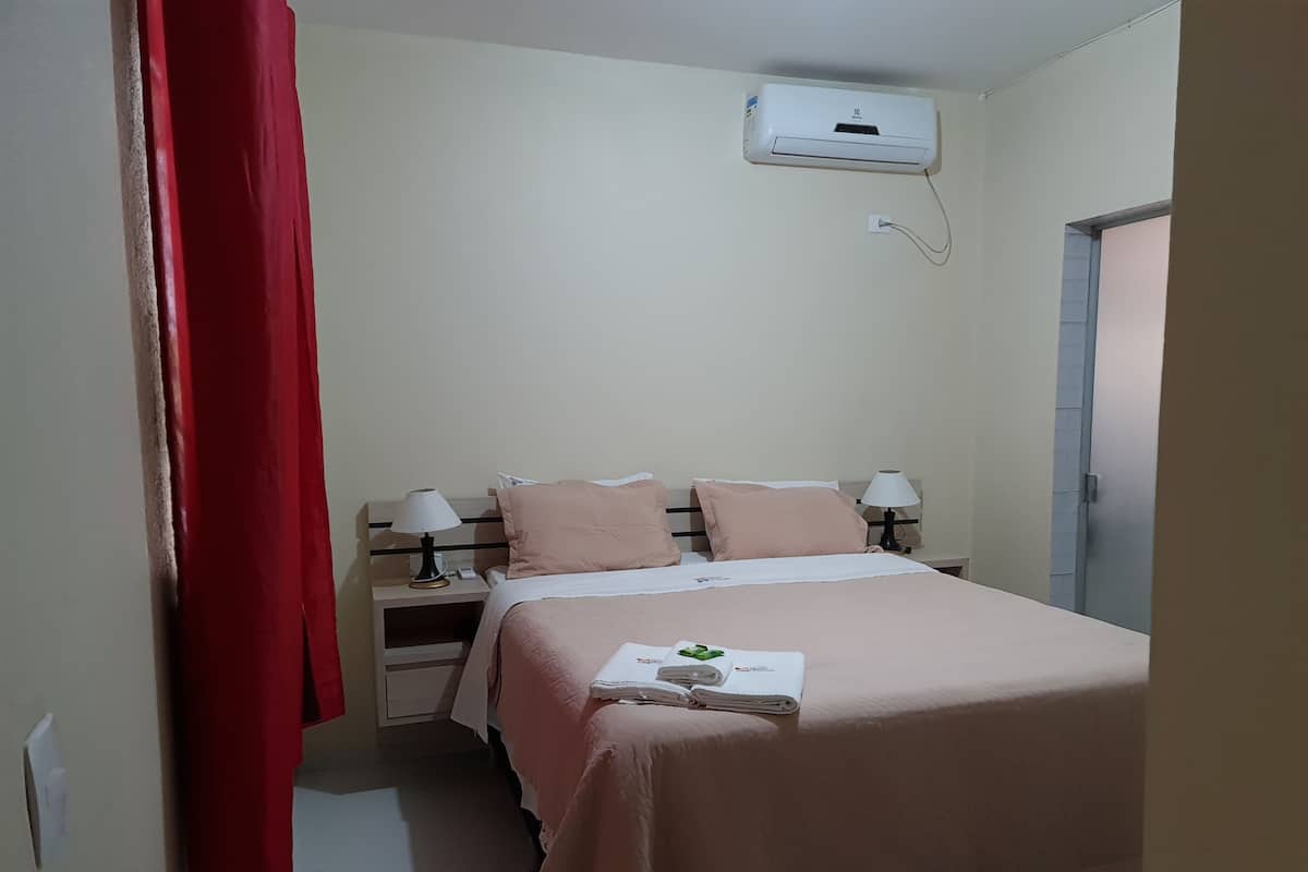 Een slaapkamer met een bed, twee nachtkastjes, een rood gordijn, een airconditioning en een deur.