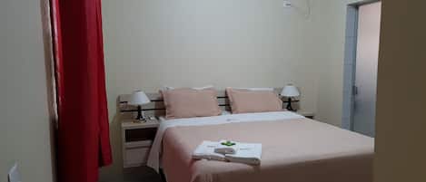 A bedroom with a bed, two bedside tables, a red curtain, an air conditioning unit, and a door.