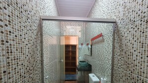 Une salle de bain avec des murs recouverts de mosaïques, une porte en verre, des toilettes, un lavabo et un espace douche.
