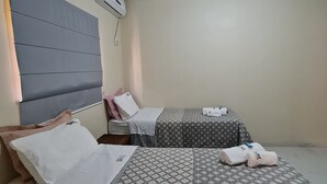 Une chambre d’hôtel avec deux lits, une tête de lit, une table de chevet, un climatiseur fixé au mur et un luminaire au plafond.