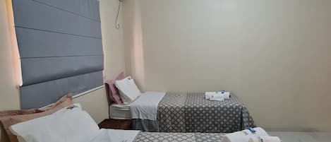 A hotel room with two beds, a headboard, a bedside table, a wall-mounted air conditioner, and a ceiling light.