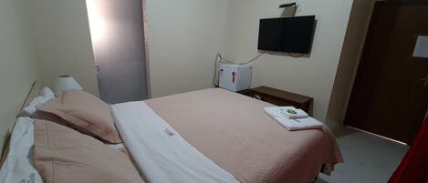 A bedroom with a bed, a desk, a television, and a door.