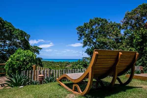 A wooden rocking chair in a lush garden with a wooden fence, overlooking a scenic view of the ocean.