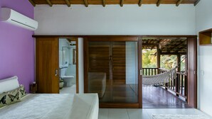 A bedroom with a bed, a wooden door leading to a balcony, and a bathroom with a toilet and sink. - Morena Casa & Hotel (Trancoso)