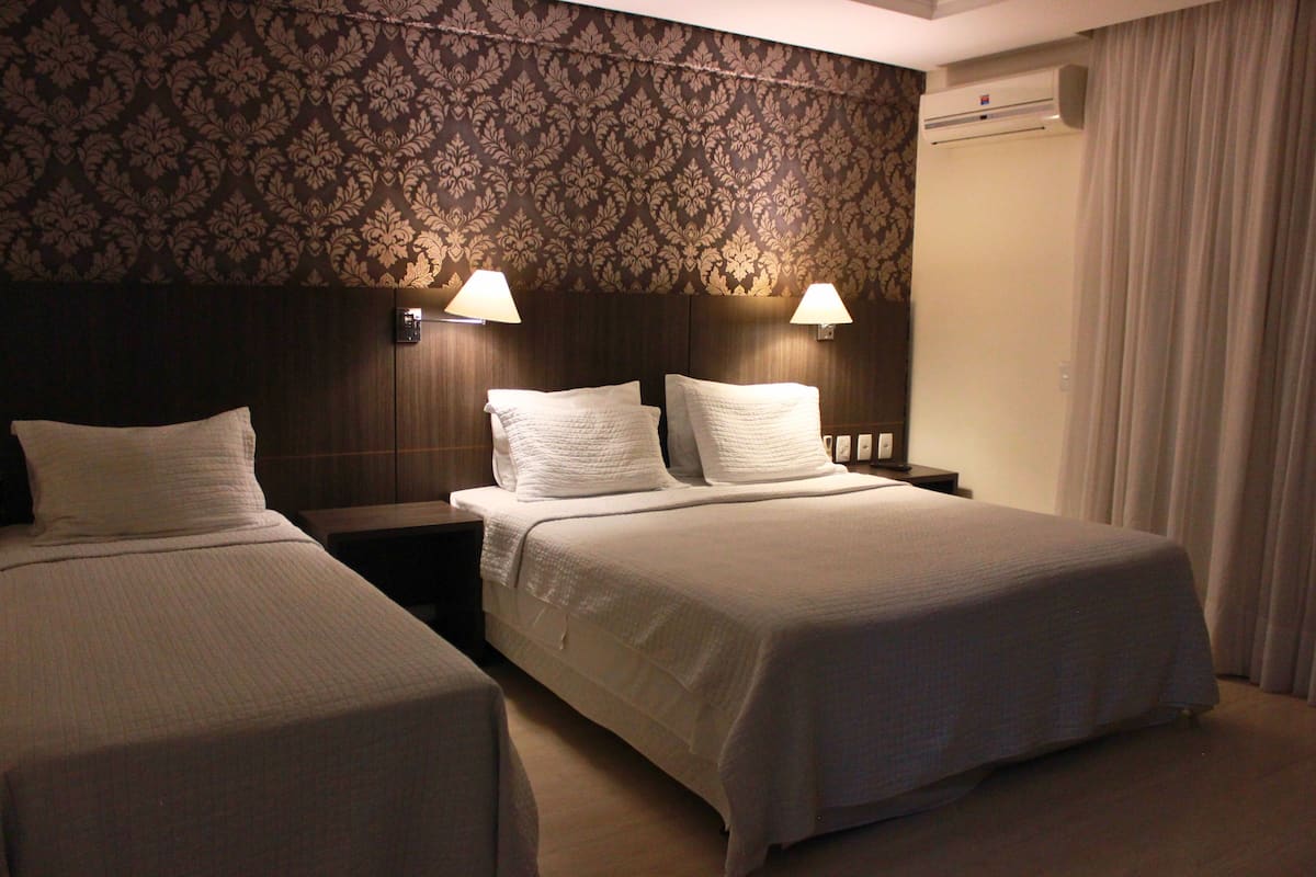 Een hotelkamer met twee eenpersoonsbedden, een nachtkastje met een lamp en behang met een patroon.