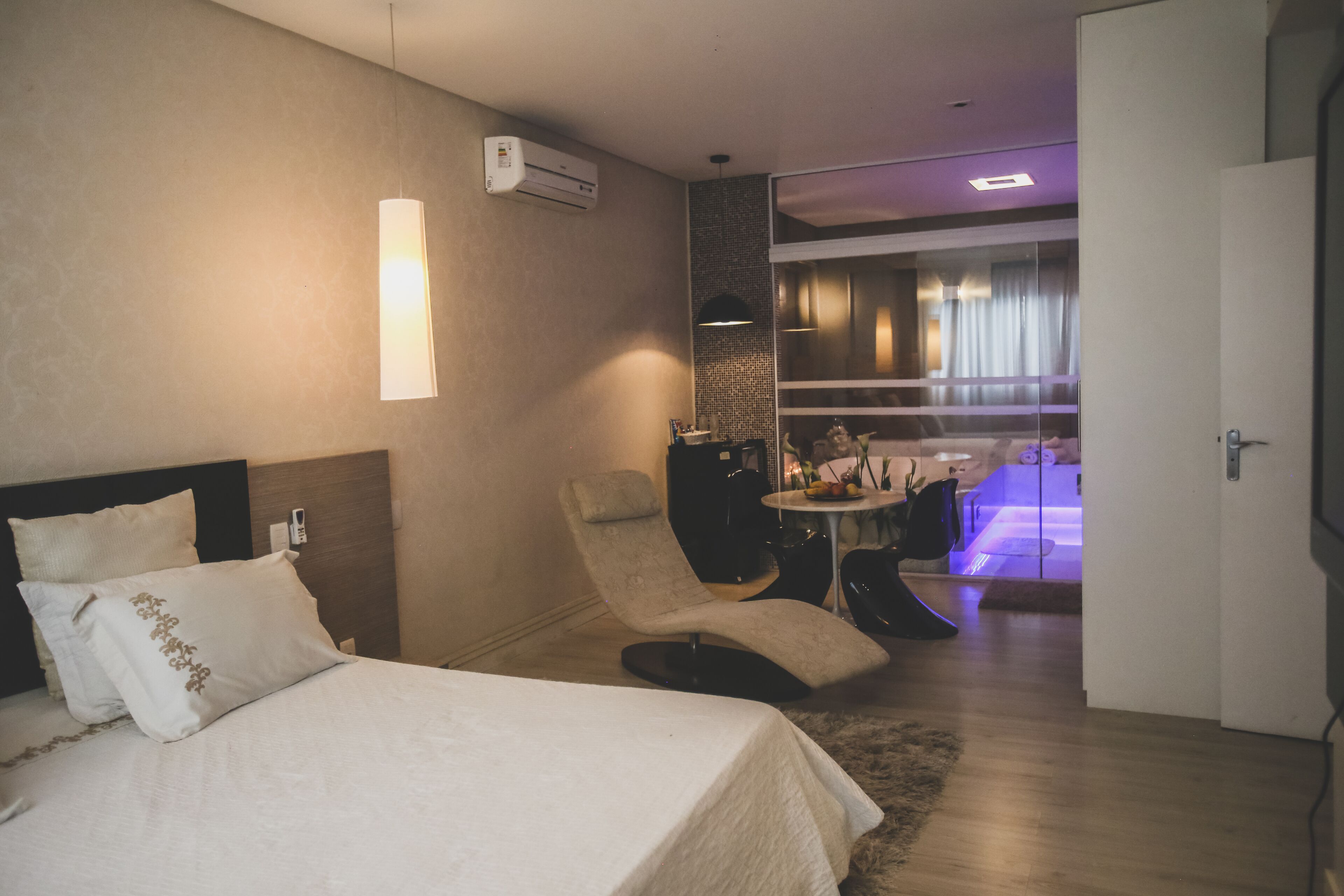 A hotel room with a bed, a chair, a small table, and a sliding door leading to a balcony.