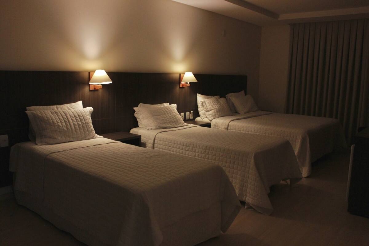 Een hotelkamer met twee bedden, elk met hoofdbord en nachtkastjes. Boven de bedden hangen wandlampen.