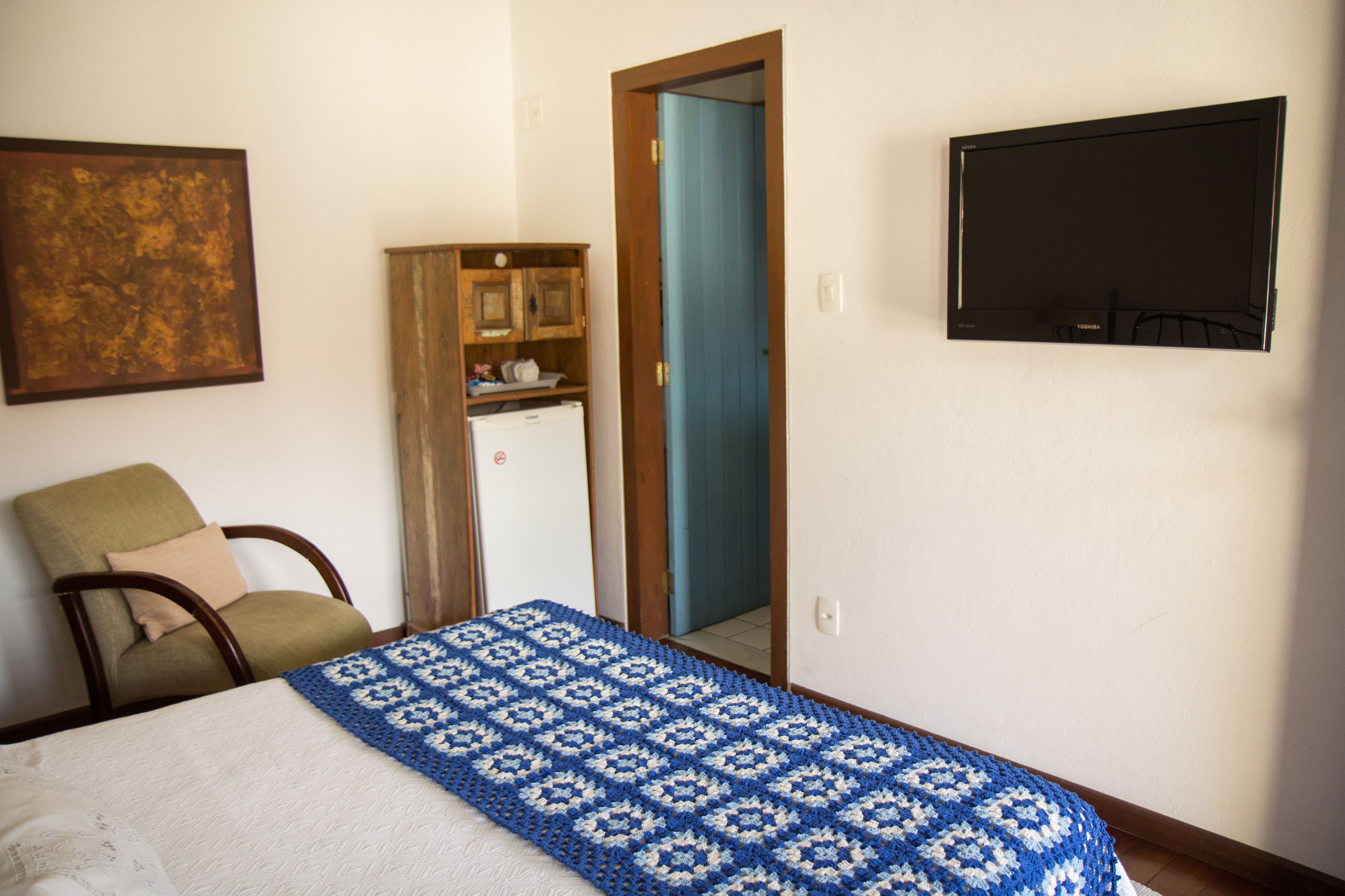 Une chambre avec un lit, une chaise, un petit réfrigérateur et un téléviseur fixé au mur.
