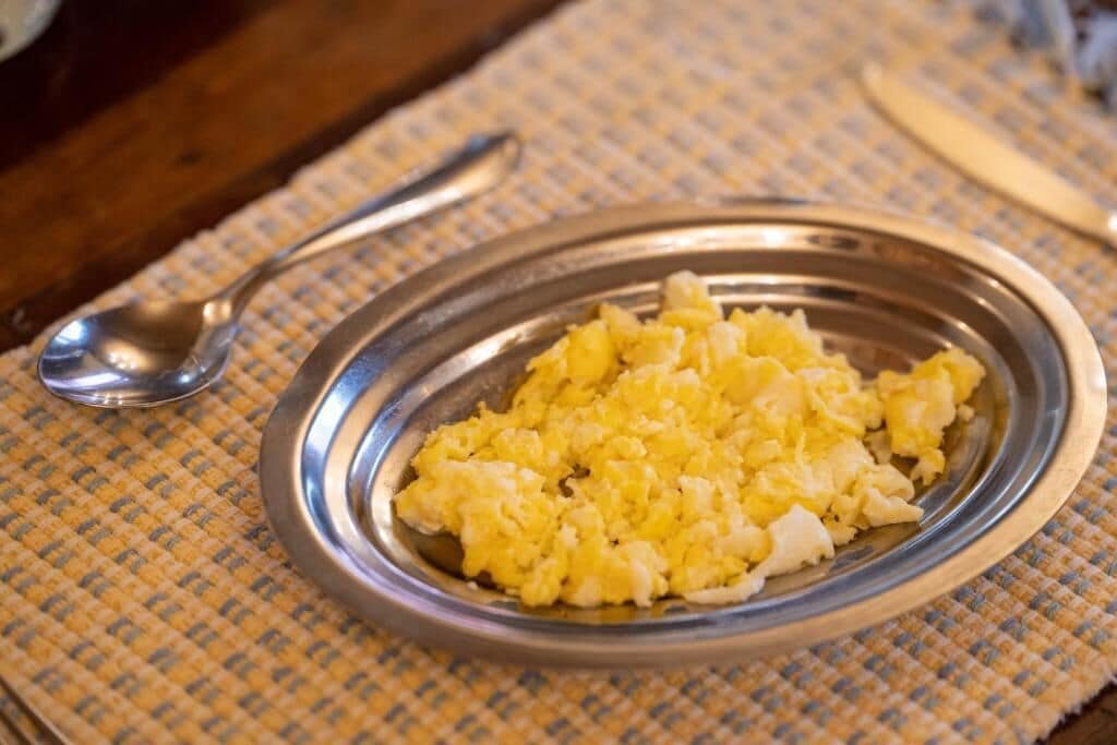 A metal plate with scrambled eggs on a woven placemat.