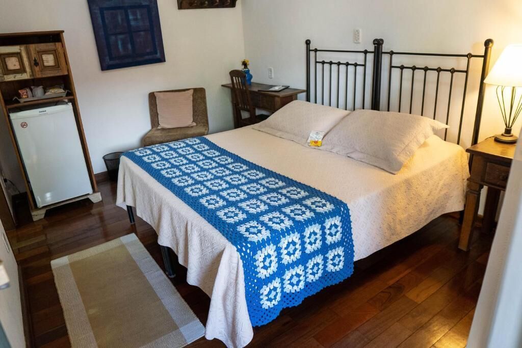 Une chambre comprenant un lit, une table de chevet, un bureau, une chaise, un petit réfrigérateur et une étagère fixée au mur.