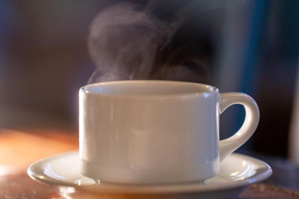 A white cup with steam rising from it, placed on a saucer.