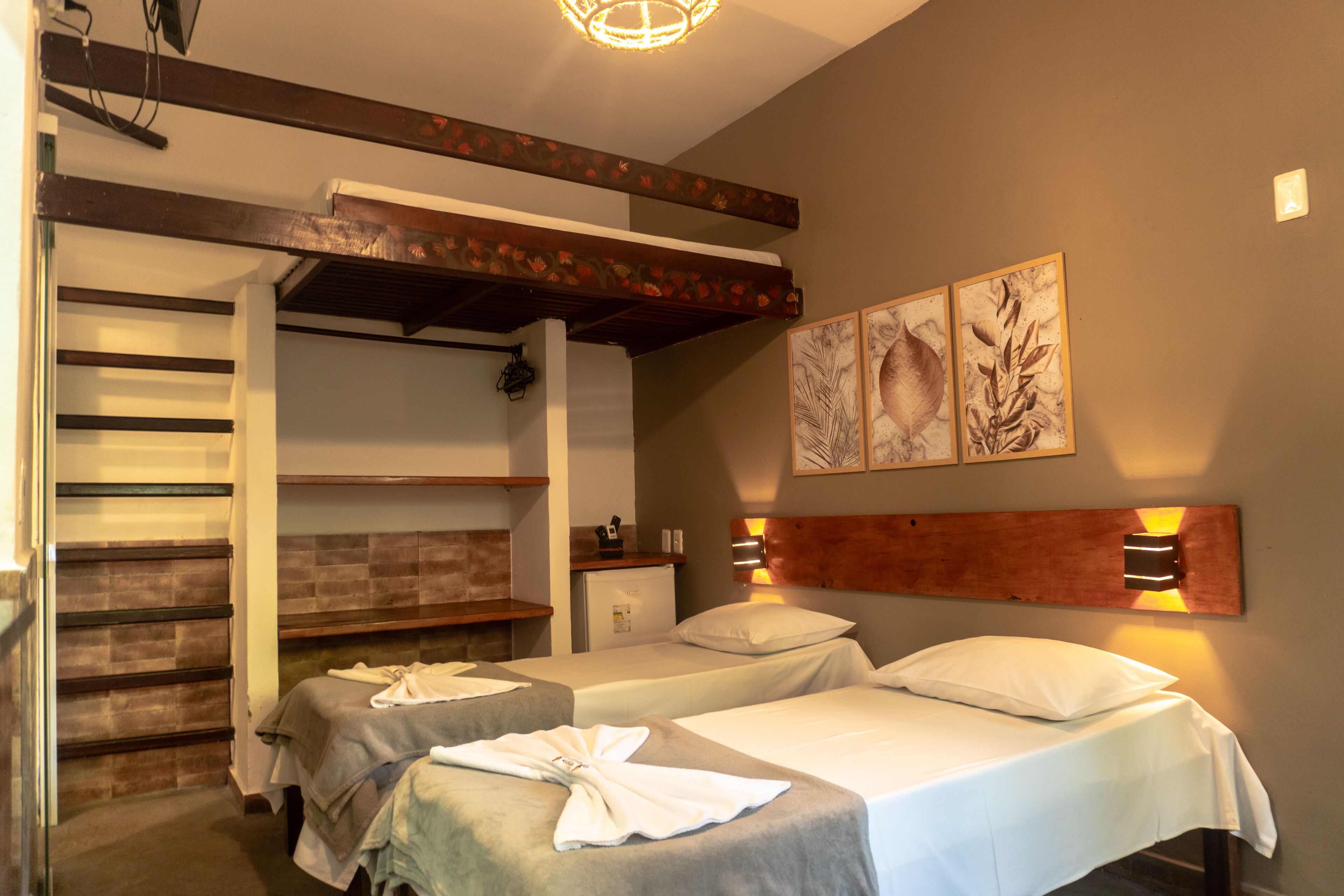 A hotel room with two beds, a built-in bench, a small refrigerator, and artwork on the wall.