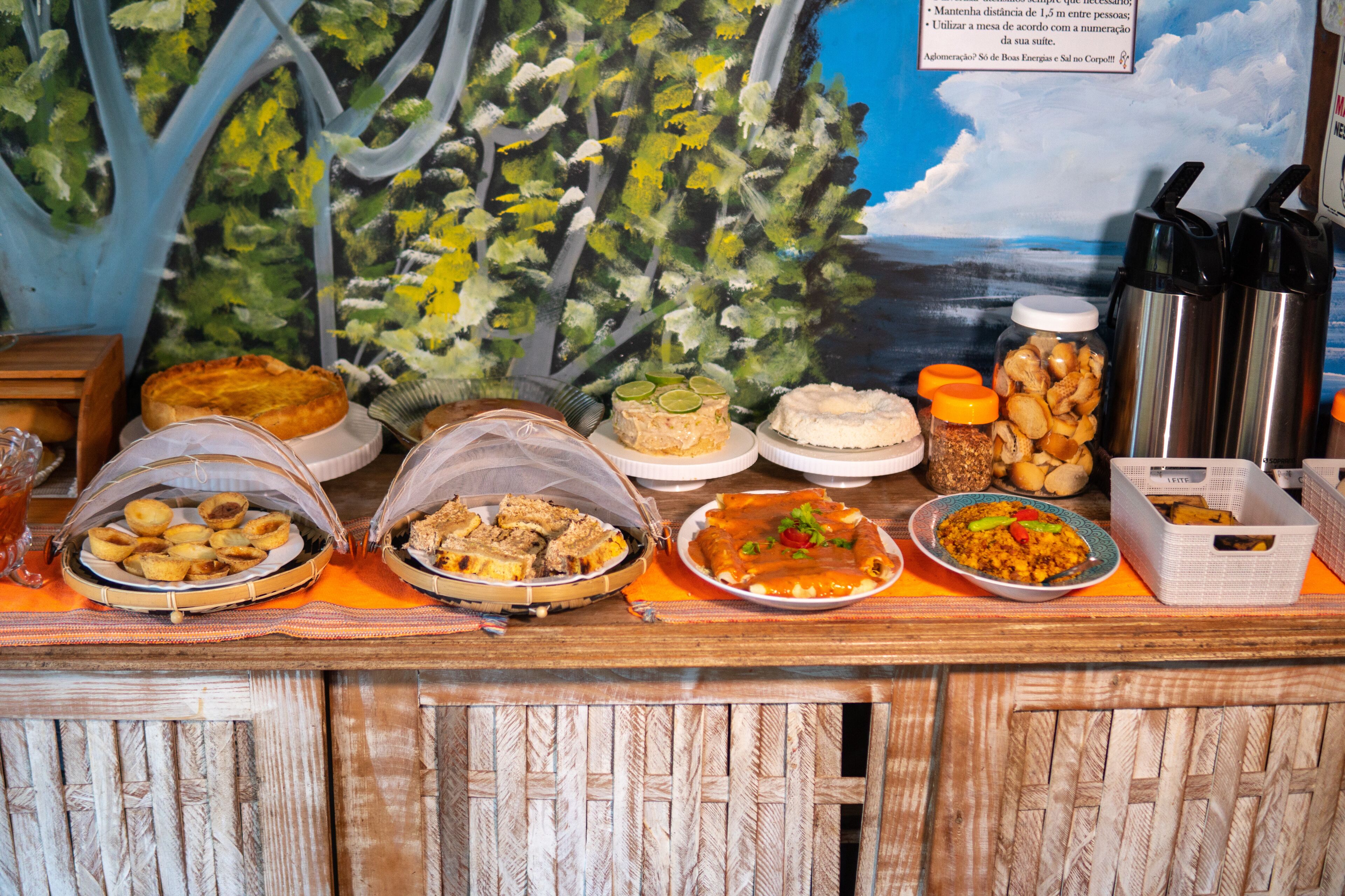 Une table de buffet proposant divers plats, avec une fresque tropicale en arrière-plan.