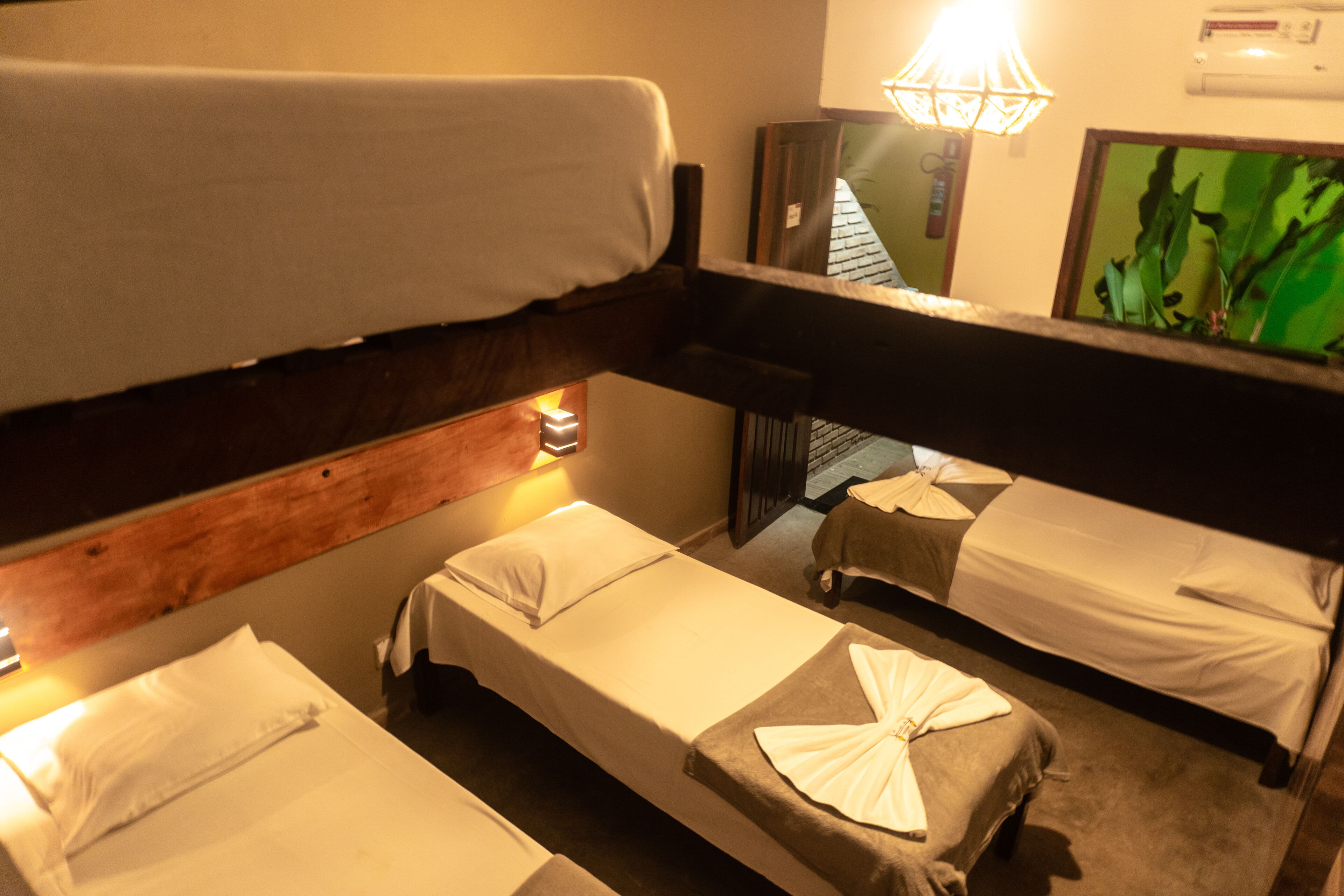 A room with bunk beds and a single bed, each with white linens. There is a wall-mounted air conditioner and a framed picture on the wall.