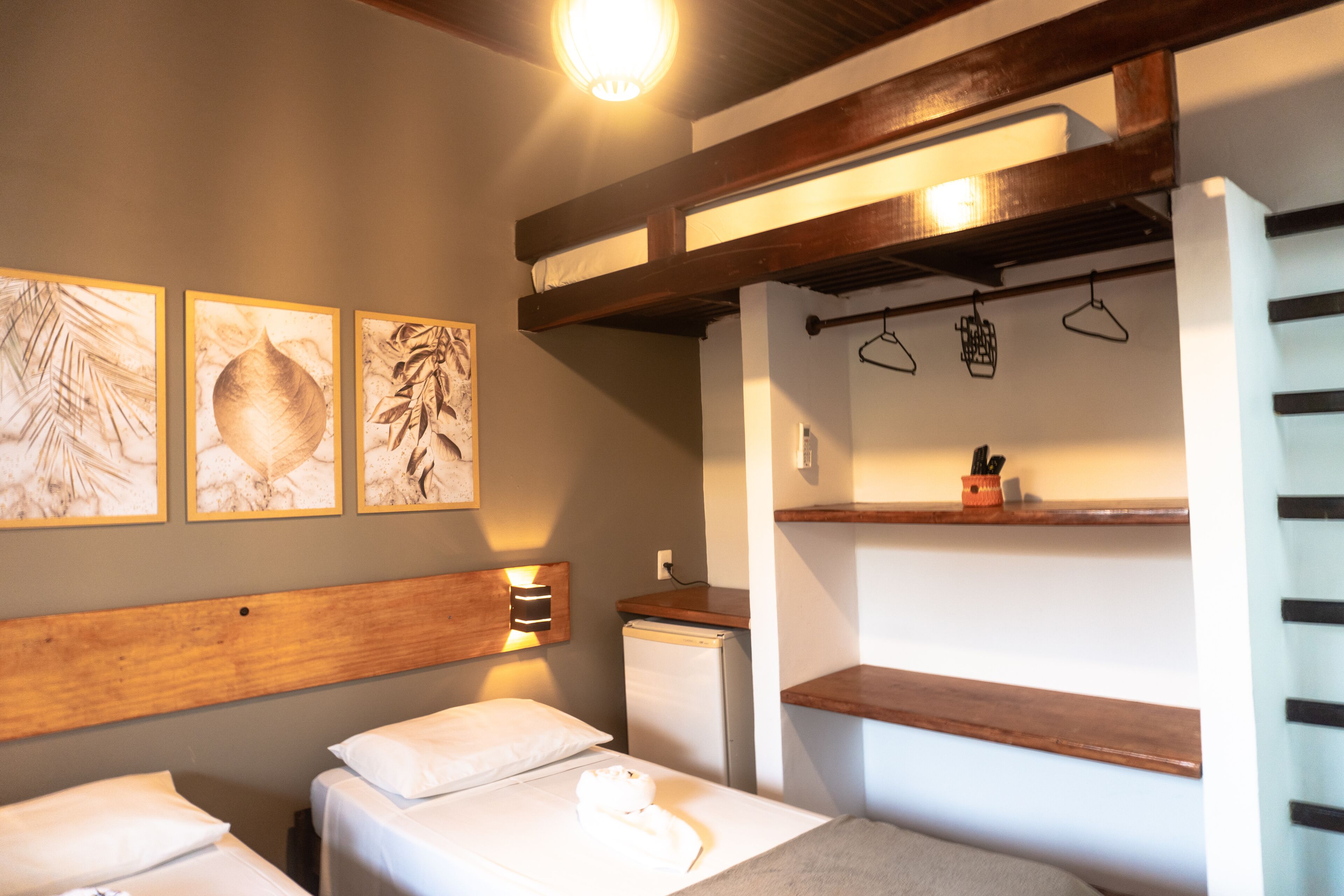 Habitación de hotel con dos camas, un refrigerador pequeño, cabeceras de madera y obras de arte colgadas en la pared.