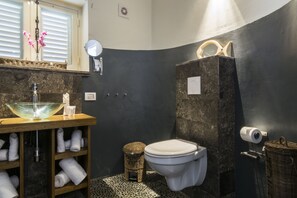 A bathroom with a glass bowl sink, a white toilet, and a dark wall.