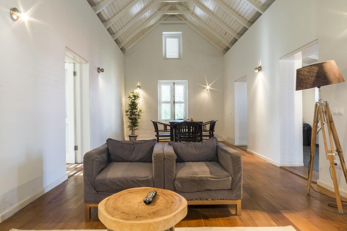 Un salon spacieux avec un plafond haut, un plancher en bois, un canapé gris, une table basse en bois et une lampe.