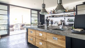 A modern kitchen with a large island, built-in appliances, and a view to an outdoor patio area. - Pietermaai Ocean Front (Willemstad)