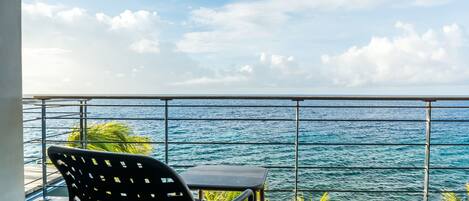 A balcony with a view of the ocean, a chair, and a table.