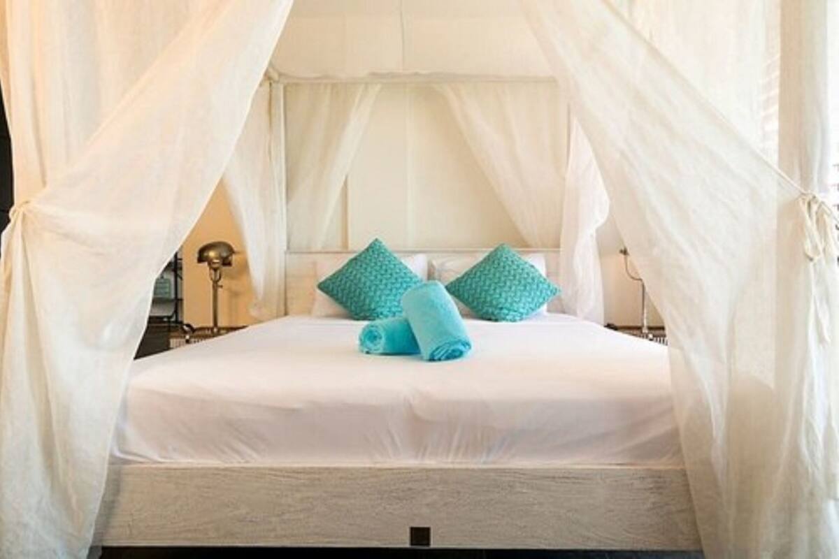 A bed with white bedding and a canopy, two pillows, and a rolled towel.