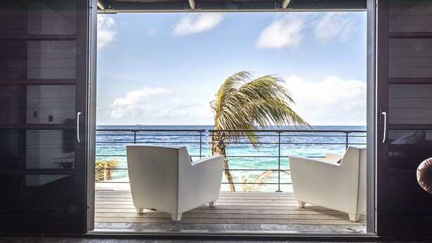 A room with a view of the ocean, two white chairs, and a palm tree. - Pietermaai Ocean Front (Willemstad)